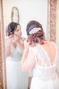 Bride adjusts her earrings in the mirror on her wedding day