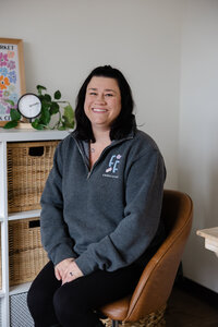 Woman with dark hair in gray sweater seated in studio portrait. Photograph by Yucaipa branding photographer Kaitlyn Dawn Photography.