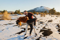 Man playfully twirling his partner in the snow at sunset during their engagement session