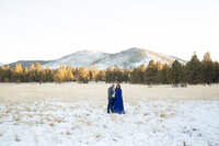 Bride in a navy blue dress standing alone in a snowy field during her Flagstaff elopement