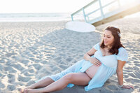 expecting mother laying down on the beach in Santa Monica in a long flowy dress