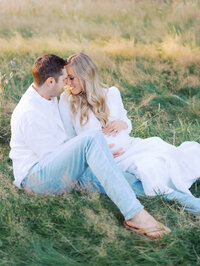 Pregnant woman and her husband are sitting on the ground and embracing
