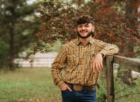Senior portrait at Circle B Lake in Wilmer, Alabama — leaning against a wooden fence in a
yellow flannel shirt and jeans.
