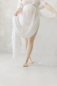 A portrait maternity session taken in a Dallas/Fort Worth area photography studio of an expecting mother from the chest down while she is dancing playfully in the studio.