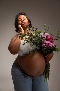 Woman posing with baby bump and a bundle of flowers.