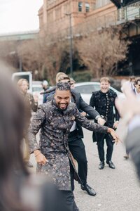 A man in a floral patterned suit smiling and reaching out while walking through a crowd of cheering people.