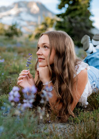 Girl laying in the grass with purple wildflowers for her senior portraits at Mount Hood's Timberline Lodge.