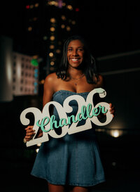 Senior portrait in downtown Mobile, Alabama — holding a white wooden “2026” sign for her
class year.