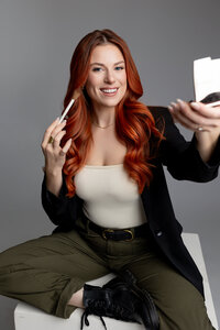 Woman with red hair holding mascara and compact mirror while seated at a table. Photograph by Yucaipa branding photographer Kaitlyn Dawn Photography.