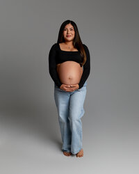 Expecting mom standing front-facing, gently holding her belly during a simple and modern maternity session by Kaitlyn Dawn Photography in Yucaipa.