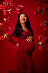 Pregnant woman in a deep red dress posing against a vivid red backdrop with floral accents, captured in a bold and modern maternity session in Waukesha.