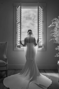 Bride standing in front of a bright window in a soft black and white wedding portrait.