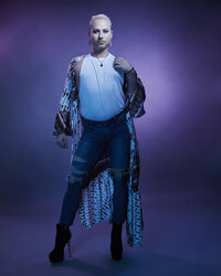 Dramatic full-body pose of Dain August in a blue sequined outfit, set against a vibrant studio backdrop, captured by Ylva Erevall.