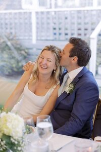 Groom kisses Bride as they laugh during reception toasts.