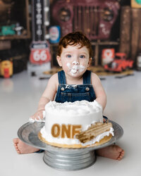 Little boy celebrating his first birthday with a cake smash, face covered in frosting and set against a retro garage theme.
Photograph by Yucaipa cake smash photographer Kaitlyn Dawn Photography.