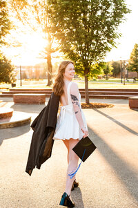 Senior walking at sunset on the MTSU campus holding robe over shoulder and smiling back at camera