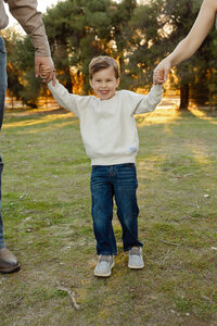 Young boy smiling while being lifted by his parents in a sunlit field, candid lifestyle family moment photographed by Kaitlyn Dawn Photography, outdoor family photographer.