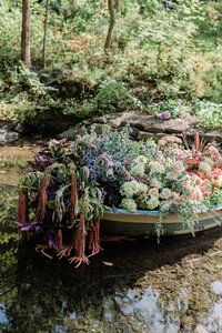Several floral arrangements sit in a boat on the water