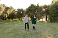 Couple walking together through a grassy park at sunset holding hands, candid outdoor portrait session photographed by Kaitlyn Dawn Photography.