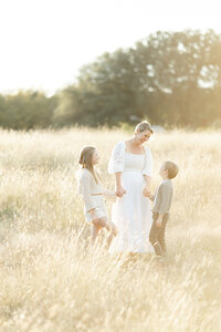 A mother holding the hands of her two children as they all stand in the middle of a field.