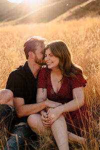 An engaged couple snuggles close in the field at Saddlerock Trailhead in Wenatchee, Washington.