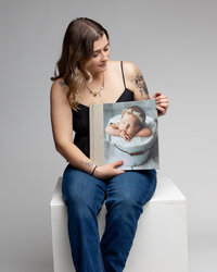 Photographer holding a custom newborn album featuring a sleeping baby portrait, Kaitlyn Dawn Photography, Yucaipa newborn photographer.