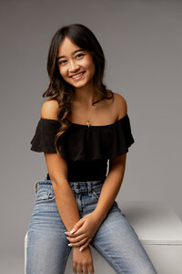 High school senior girl sitting in a studio wearing a black off-shoulder top and patterned pants, senior portrait by Kaitlyn Dawn Photography.