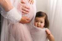 Toddler peers at the camera during her mother's Studio Maternity Photoshoot in Charleston, SC