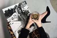 Image of a woman wearing leopard print trousers and black stilettos holding a coffee with a high end fashion/photography magazine on her lap