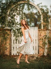 Senior portrait in downtown Magnolia Springs, Alabama — twirling her dress in front of a white picket fence.