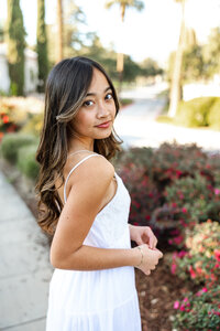 High school senior girl posing on a garden path with flowers and greenery, senior photography session by Kaitlyn Dawn Photography.