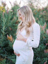 Pregnant woman smiling and looking at a flowering tree in front of her while holding her stomach