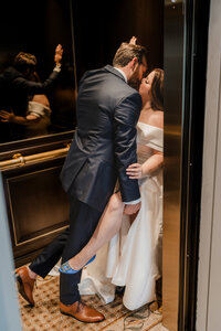 Mariés s'embrassant avec passion dans un ascenseur doré, mariée soulevant sa jambe ornée de souliers bleus, boiseries élégantes au Ritz-Carlton Montréal