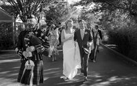 Couple smile as they walk with their guests down the road to their wedding reception.