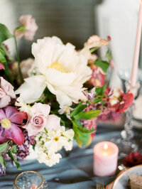 close-up of white peonies and delicate flowers arranged with candles on a dusty blue linen wedding table