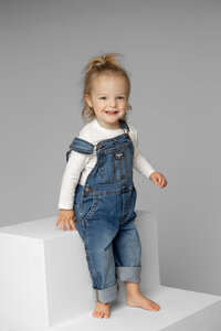 Toddler girl standing on modern white studio steps in a neutral gray setting, natural light child portrait captured by Kaitlyn Dawn Photography, children’s photographer.