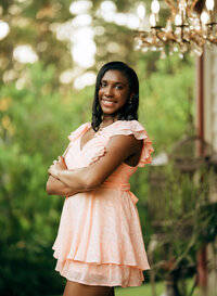 Senior portrait at Bella Sera Gardens in Loxley, Alabama — arms crossed beneath a vintage
chandelier with greenery behind her.