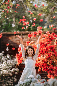 Child in white lace dress tossing pink and white flowers in a blooming spring garden