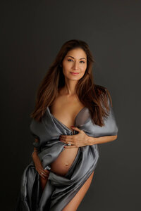 close up portrait of smiling pregnant woman wrapped in fabric during fine art maternity portrait session in North Hollywood, dark moody setting