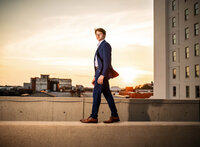 Senior portrait in downtown Mobile, Alabama— walking on a cement barrier while the wind blows the tail of his dress suit, creating a dramatic effect.