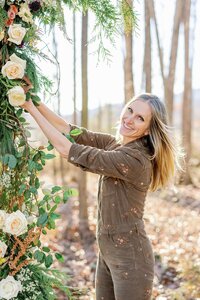 Founder of Flowergirl Cville and Maison Charlottesville, Jennifer Blanchet arranging flowers on a wedding arch.