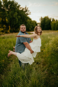 Couple posing playfully in open field during casual golden hour engagement photo session.