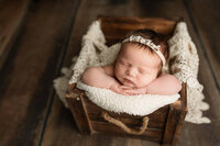 Baby girl safely posed in a wooden crate during her newborn session near Mankato, MN with Jennifer Brandes photography.
