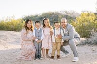 The Collins family posing together in the Las Vegas desert at golden hour, with parents and three children smiling closely for a bright, natural outdoor family portrait session.