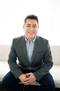 Contemporary headshot portrait of a man in a suit sitting on a white couch at our Waukesha studio.