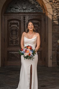 Bride smiling with her colorful bouquet outside on her wedding day in New England.
