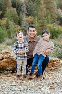 Father sitting on a fallen log with his two young sons in a mountain setting, natural earthy tones and relaxed expressions photographed by Kaitlyn Dawn Photography, lifestyle family photographer.