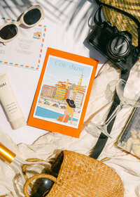 Styled product photography flat lay featuring travel-inspired artwork, accessories, and lifestyle props for editorial brand storytelling
