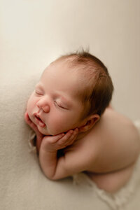 A baby posed on white fabric holding his face.
