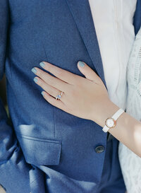Lady with a wedding ring, blue nail polish, and a classic white watch puts her hand on a gentleman's chest.